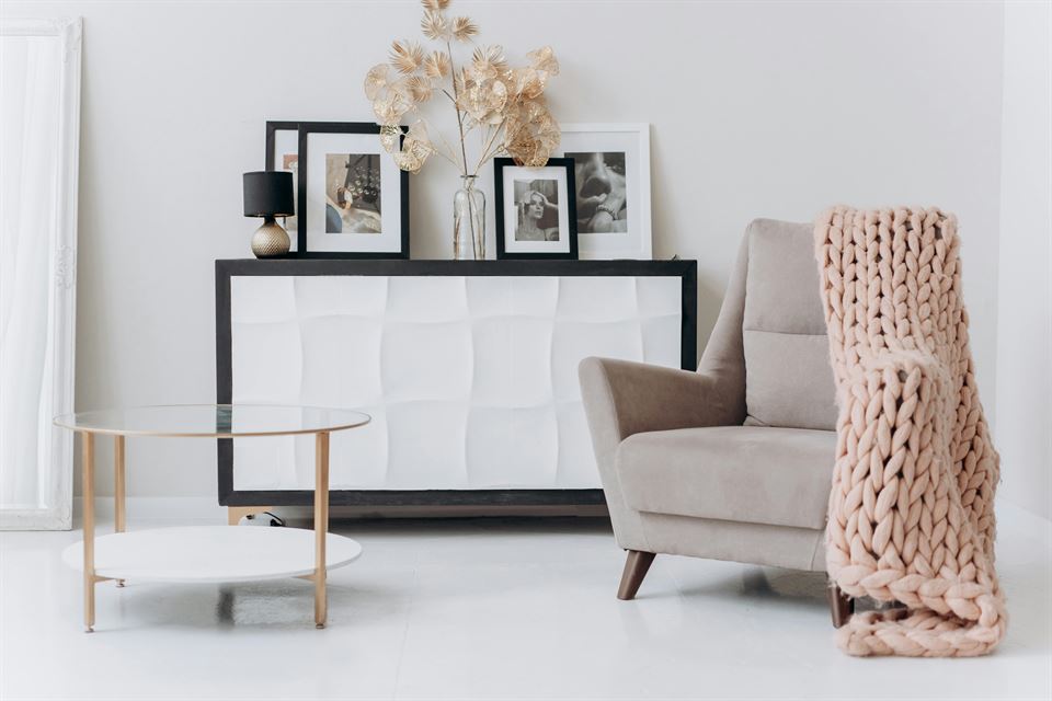 mueble-blanco-con-fotos-sofa-beige-con-manta-rosa-y-paredes-y-mesa-blancas